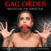 Woman wearing a red silicone ball gag with black adjustable strap, hands raised, against a black textured background.