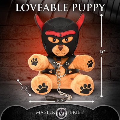 Light peach plush bear wearing a black and red puppy mask and faux leather harness with chain leash, sitting against a brick wall background.