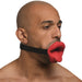 Man wearing a red vibrating lips mouth gag with a tongue design and adjustable black strap against a white background.