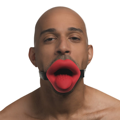 Man wearing a red vibrating lips mouth gag with tongue detail and adjustable black strap.