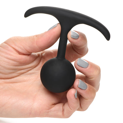 Hand holding a small black silicone weighted anal plug with a round bulb and slim T-shaped base.