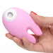 Hand holding a pink silicone clitoral stimulator with dual bunny ear design and a white suction opening.