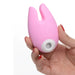 Hand holding a pink silicone clitoral stimulator with dual bunny ear design and white suction opening.