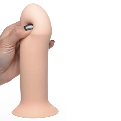 Hand squeezing a beige, thick, flexible silicone dildo with suction base against a white background.
