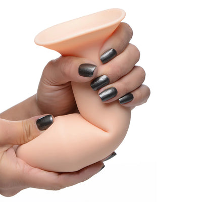 Hands squeezing and bending a beige, thick, flexible silicone dildo with a suction cup base against a white background.