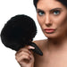 Woman holding a black interchangeable bunny tail with a soft fluffy texture and silicone base near her face.