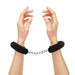 Hands wearing black furry handcuffs connected by a silver metal chain against a white background.