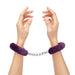 Hands wearing purple furry handcuffs connected by a silver metal chain on a white background.