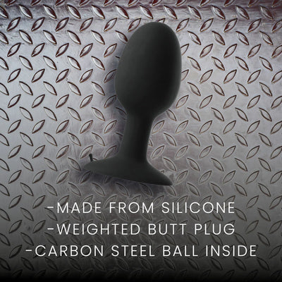 Black silicone weighted butt plug with a tapered shape and flared base on a textured metal surface background.