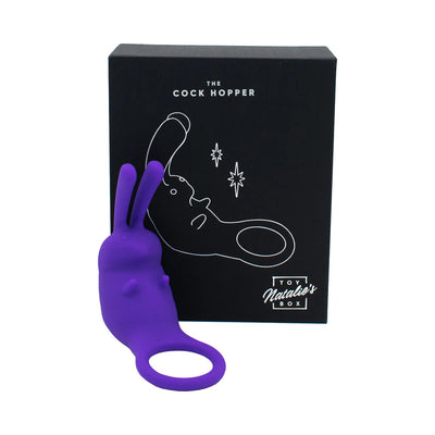 Purple silicone cock ring with twin-tip rabbit vibrator displayed in front of black packaging box.