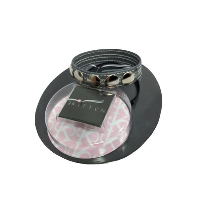 Black leather adjustable ring with five silver snap buttons displayed on branded packaging.