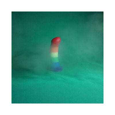Rainbow-colored silicone dildo with suction base standing upright on a green surface with misty background.