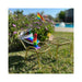 Rainbow silicone dildo displayed on a small gold chair outdoors with a matching table and a drink with lemon garnish.
