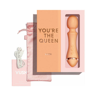 Peach-colored Majesty 2 wand vibrator in pink box with "You're the Queen" text, USB charging cable, satin pouch, and user manual.