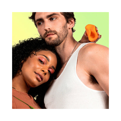 Couple posing with the orange VUSH Sol Vibrating Stroker held near the man's shoulder against a gradient background.
