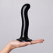 Hand holding a black silicone dildo with a curved shape and suction cup base against a neutral background.