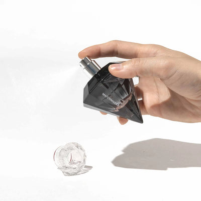 Hand spraying Eye of Love Matchmaker Black Diamond pheromone perfume in a black diamond-shaped bottle with clear cap on white background.
