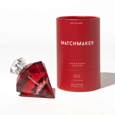 Red diamond-shaped perfume bottle with clear cap next to matching red cylindrical packaging for Matchmaker pheromone parfum.