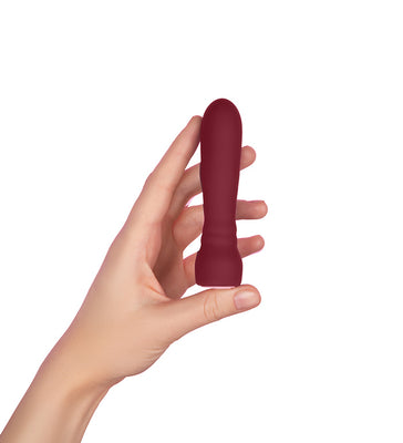 Hand holding a compact, smooth purple silicone massager with a rounded tip against a white background.