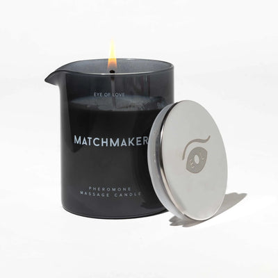 Eye of Love Matchmaker black glass massage candle with lit wick and silver lid on white background