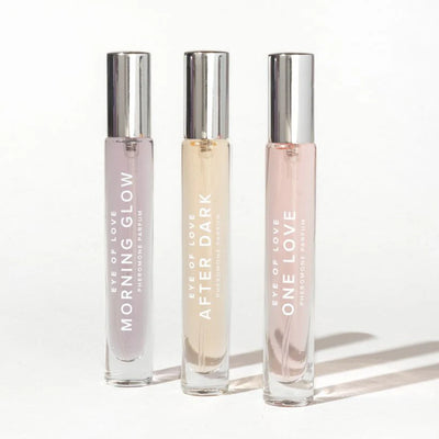 Set of three Eye of Love pheromone perfumes in slender glass bottles with silver caps, labeled Morning Glow, After Dark, and One Love.