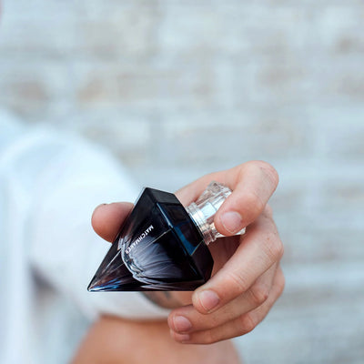 Hand holding Eye of Love Matchmaker Pheromone Perfume in a black diamond-shaped bottle with clear cap.