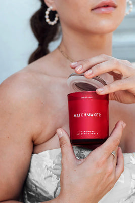 Close-up of a woman holding the red Eye of Love Matchmaker Pheromone Massage Candle with the lid open.