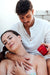 Couple sharing a relaxing moment with a red Eye of Love Matchmaker Massage Candle in hand.