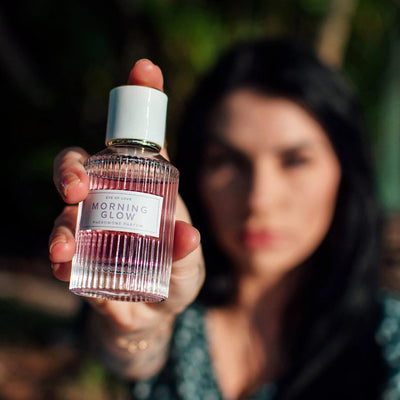 Woman holding Eye of Love Morning Glow pheromone perfume bottle with pink liquid and white cap outdoors