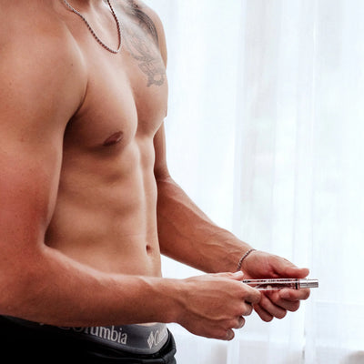 Shirtless man holding a slim 10ml Eye of Love Pheromone Perfume bottle near a bright window.