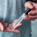 Hand holding a 10ml clear glass bottle of Eye of Love Unscented Pheromone Perfume with black cap.