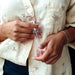 Hands holding a slim clear bottle of Eye of Love Unscented Pheromone Perfume against a floral patterned shirt background.
