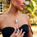 Woman in black strapless top holding Eye of Love One Love pheromone perfume bottle near her chest outdoors