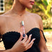 Woman in black dress holding Eye of Love One Love pheromone perfume bottle against her chest outdoors