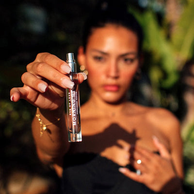 Woman holding Eye of Love Morning Glow pheromone perfume spray bottle outdoors in natural light