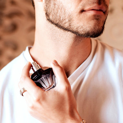 Man applying Eye of Love Matchmaker Pheromone Perfume Black Diamond cologne from a stylish glass bottle.