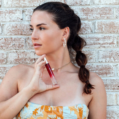 Woman with braided hair holding Eye of Love Matchmaker Pheromone Perfume Red Diamond against a brick wall background.