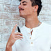Man in white henley shirt enjoying scent from black spray perfume bottle against brick wall background