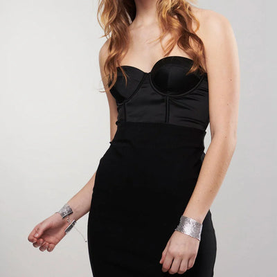 Woman wearing elegant black dress with Bijoux Indiscrets Desir Metallique silver mesh handcuff bracelets connected by a chain.