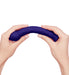 Hands bending a flexible, textured deep purple silicone pleasure wand against a white background.