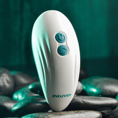 White oval-shaped Evolved Palm Pleasure vibrator with blue control buttons resting on smooth black stones.