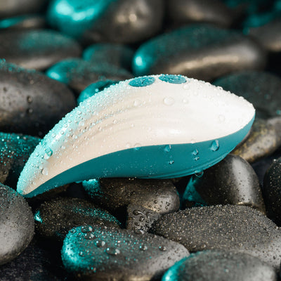 Evolved Palm Pleasure waterproof vibrator with water droplets resting on black spa stones.