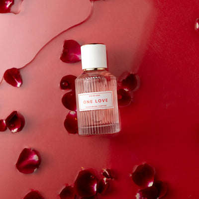 Eye of Love One Love pheromone perfume bottle on red surface with scattered rose petals.