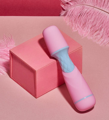 Compact pink and blue Femme Funn Ffix Mini Wand vibrator displayed on a pink box with soft pink feathers nearby.