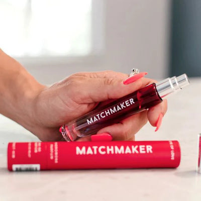 Hand holding Eye of Love Matchmaker pheromone perfume spray with red packaging on white surface