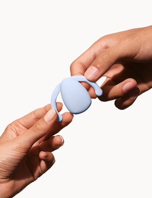 Hands holding a light blue Dame Eva hands-free wearable vibrator against a white background.