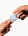 Hands holding a light blue Dame Eva hands-free wearable vibrator against a white background.