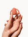 Hands holding a compact, coral-colored Dame Eva hands-free wearable vibrator against a white background.