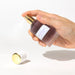 Hand holding and spraying Eye of Love Morning Glow pheromone perfume bottle with gold and white cap on white background.