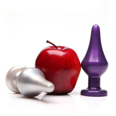 Two metallic toadstool-shaped plugs in silver and purple next to a red apple on a white background.